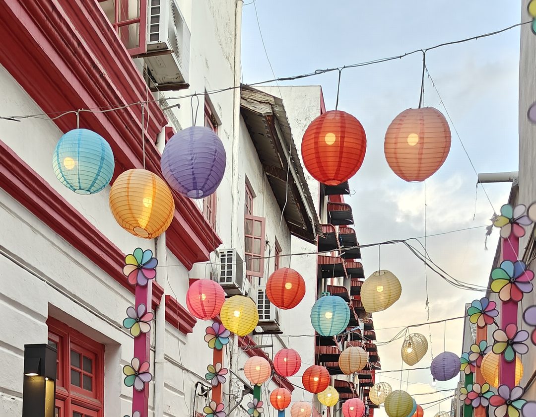 Pastel paper lanterns strung over a shophouse street